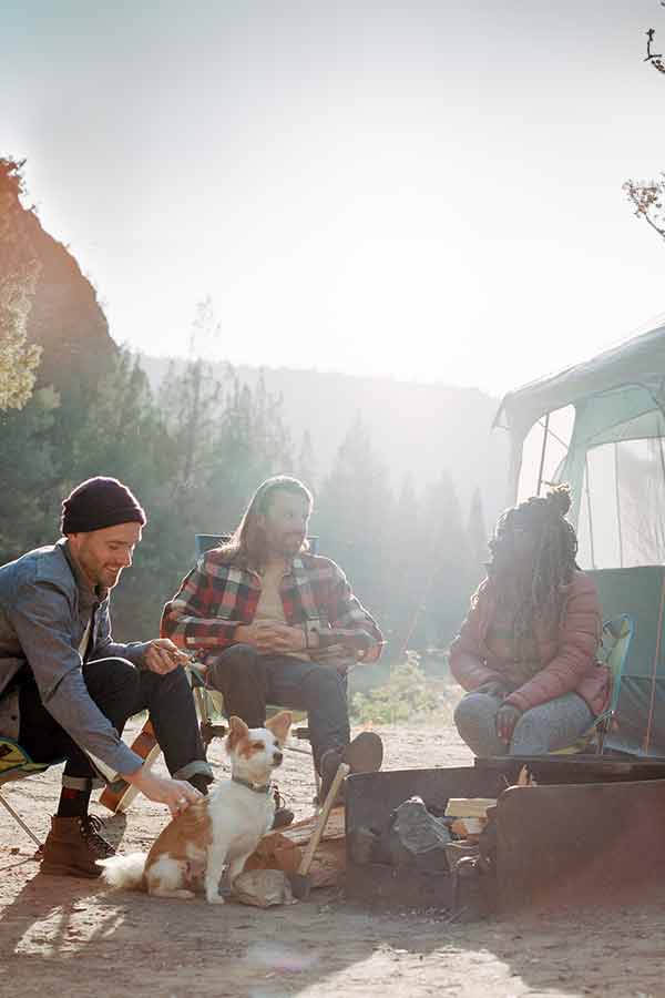 Three adults with small dog sitting in camp chairs next to text
