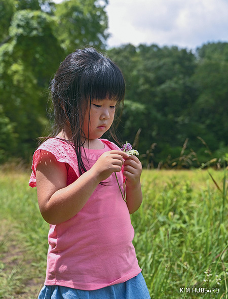 Child (female) plays with wildflowers at the Reflection Riding Nature Center summer camp