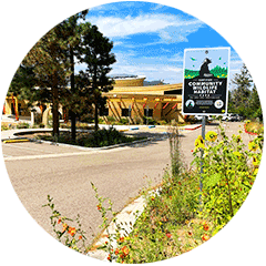 A Certified Community Wildlife Habitat sign installed at the entry road into a building complex surrounded by trees and flower beds.